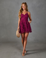 Woman wearing magenta lace floral romper with spaghetti straps, clear heeled sandals, holding woven clutch bag