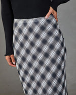 Gray plaid bias-cut midi skirt paired with black ribbed long-sleeve top, worn by woman with gold rings