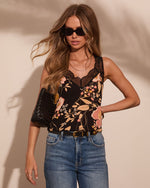 Woman wearing black floral lace cami top with high-waist jeans, belt, sunglasses, and woven clutch bag
