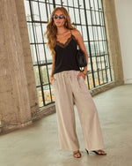 Woman wearing black lace cami top, beige striped wide-leg pants, black heeled sandals, gold jewelry, and small black clutch bag.