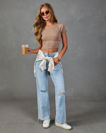 Woman in taupe ribbed crop top, light wash ripped wide-leg jeans, white sneakers, holding iced coffee, cream jacket tied at waist