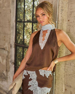 Woman in brown satin halter top and matching skirt with light blue lace trim, styled with gold cuff and woven clutch