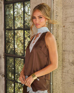 Woman in brown satin sleeveless top with light blue lace trim and matching skirt, styled with gold cuff bracelet and earrings