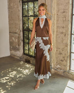Woman in a brown satin midi dress with light blue lace trim and a halter neckline, styled with clear heels and a woven clutch