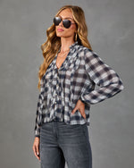 Women's plaid ruffle button-down blouse in navy gray, styled with dark jeans and aviator sunglasses, long sleeve top