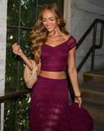 Woman wearing burgundy lace crop top and maxi skirt two-piece set, holding beige woven clutch, smiling outdoors