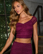 Woman wearing burgundy lace crop top and matching skirt set with cap sleeves, styled with gold layered necklaces