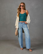 Woman wearing teal ribbed crop cami, cream cable-knit cardigan, wide-leg light wash jeans, nude strappy heels, and sunglasses