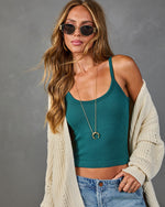 Woman wearing teal ribbed crop tank top, cream knit cardigan, jeans, gold crescent necklace, and oval sunglasses