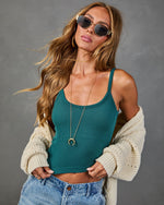 Woman wearing teal ribbed crop tank top, cream knit cardigan, jeans, gold necklace, and oval sunglasses