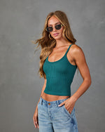 Woman wearing teal ribbed crop tank top with spaghetti straps and light wash straight-leg jeans, styled with gold hoop earrings and small oval sunglasses