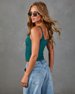 Woman wearing teal ribbed crop tank top and light wash wide-leg jeans, styled with gold sunglasses and hoop earrings