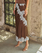 Brown satin midi skirt with white lace appliqué and lace hem, styled with clear-strap nude heels and a gold cuff bracelet