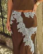 Brown satin midi skirt with white floral lace appliqué, styled with a matching top and gold cuff bracelet