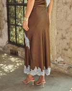 Brown satin midi skirt with white lace trim at hem and side, styled with gold cuff bracelet and nude heeled sandals