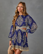 Navy blue and gold baroque floral print mini dress with balloon sleeves and cutout waist, modeled by woman holding woven clutch