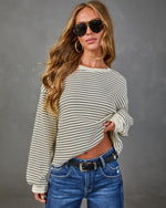 Woman wearing cream and navy striped ribbed knit long sleeve top with blue jeans, black belt, hoop earrings, and aviator sunglasses