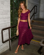 Woman wearing magenta lace two-piece crop top and maxi skirt set with nude sandals and woven clutch bag