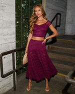 Woman wearing purple lace two-piece crop top and midi skirt set with nude heels, holding clutch bag