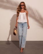 Woman in white lace cami top, light wash ripped straight-leg jeans, nude heels, holding woven tote bag, summer outfit