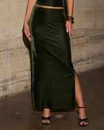 Dark green velvet maxi skirt with side slit, styled with black strappy heels and gold bangles against a concrete wall