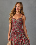 Woman wearing ruched floral midi dress in red and sage green with sweetheart neckline, gold jewelry, and woven bag
