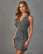 Woman wearing gray acid wash denim mini dress with V-neck, snap buttons, and raw hem, styled with gold cuff bracelet and hoop earrings