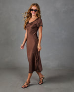 Brown satin midi dress with short puff sleeves and black trim, styled with strappy heels and sunglasses on smiling model