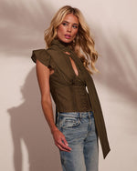 Woman wearing olive green ruffle-sleeve corset blouse with neck tie and light wash high-rise jeans