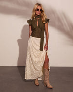 Woman in olive green ruffled blouse with neck tie, cream lace maxi skirt with slit, and tan cowboy boots