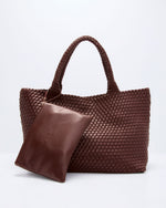 A brown woven leather tote bag with two top handles and a matching smooth leather pouch resting in front, photographed on a clean white studio background.