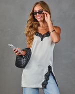 Woman wearing white satin cami top with black lace trim, paired with blue jeans, black woven bag, and cat-eye sunglasses
