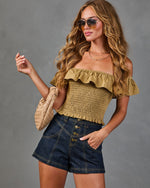 Woman wearing olive smocked off-shoulder crop top with ruffle detail, dark denim high-waist shorts, woven beige bag, aviator sunglasses