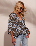 Woman wearing olive floral print boho blouse with bell sleeves and ruffle detail, paired with light wash jeans and sunglasses