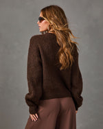 Woman in chocolate brown chunky knit sweater and wide-leg brown trousers, seen from behind with wavy hair and sunglasses