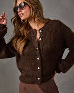Woman wearing a chocolate brown fuzzy knit cardigan with pearl buttons, oversized sunglasses, gold hoops and brown trousers