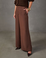 Brown high-waisted wide-leg trousers with front pleats, styled with a chocolate knit sweater, gold cuff bracelets and pointed heels