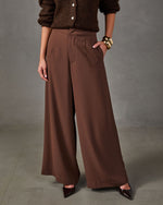 Brown high-waisted wide-leg trousers with front pleats, styled with a chunky knit cardigan, gold bracelets and pointed heels