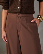 Brown high-waisted wide-leg trousers with front pleats, styled with a chunky knit brown cardigan and gold bangle bracelets