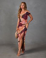 Woman wearing burgundy floral off-shoulder maxi dress with high slit, ruched waist, styled with nude heels and woven clutch