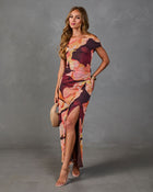 Woman wearing burgundy floral off-shoulder maxi dress with high slit, ruched waist, styled with nude heels and woven clutch