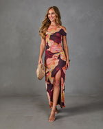 Woman wearing floral print off-shoulder maxi dress with side slit, holding woven clutch, nude heels, warm autumn tones