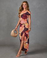 Woman wearing burgundy floral off-shoulder maxi dress with thigh slit, nude heels, and woven hobo bag
