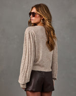 Woman in oatmeal knit sweater with textured bobble puff sleeves, brown leather shorts, aviator sunglasses and gold hoop earrings