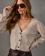 Beige pointelle knit cardigan with lace trim, blue buttons and puff sleeves, styled with aviator sunglasses and brown faux leather pants