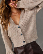 Beige pom-pom knit cardigan with blue buttons and scalloped lace trim, styled with brown leather shorts and gold jewelry