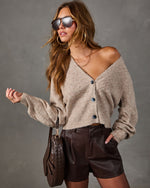 Woman in beige pointelle cardigan with lace trim, brown faux leather shorts, aviator sunglasses and woven brown shoulder bag