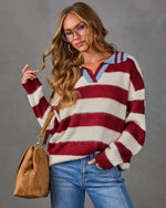 Woman wearing a red and cream striped collared sweater with blue trim, jeans, tinted glasses and a tan suede shoulder bag