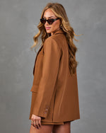 Woman wearing oversized camel brown blazer and matching shorts, styled with cat-eye sunglasses and gold jewelry, side profile view