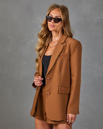 Woman wearing camel brown blazer and matching shorts set with black tank top, cat-eye sunglasses, and gold jewelry